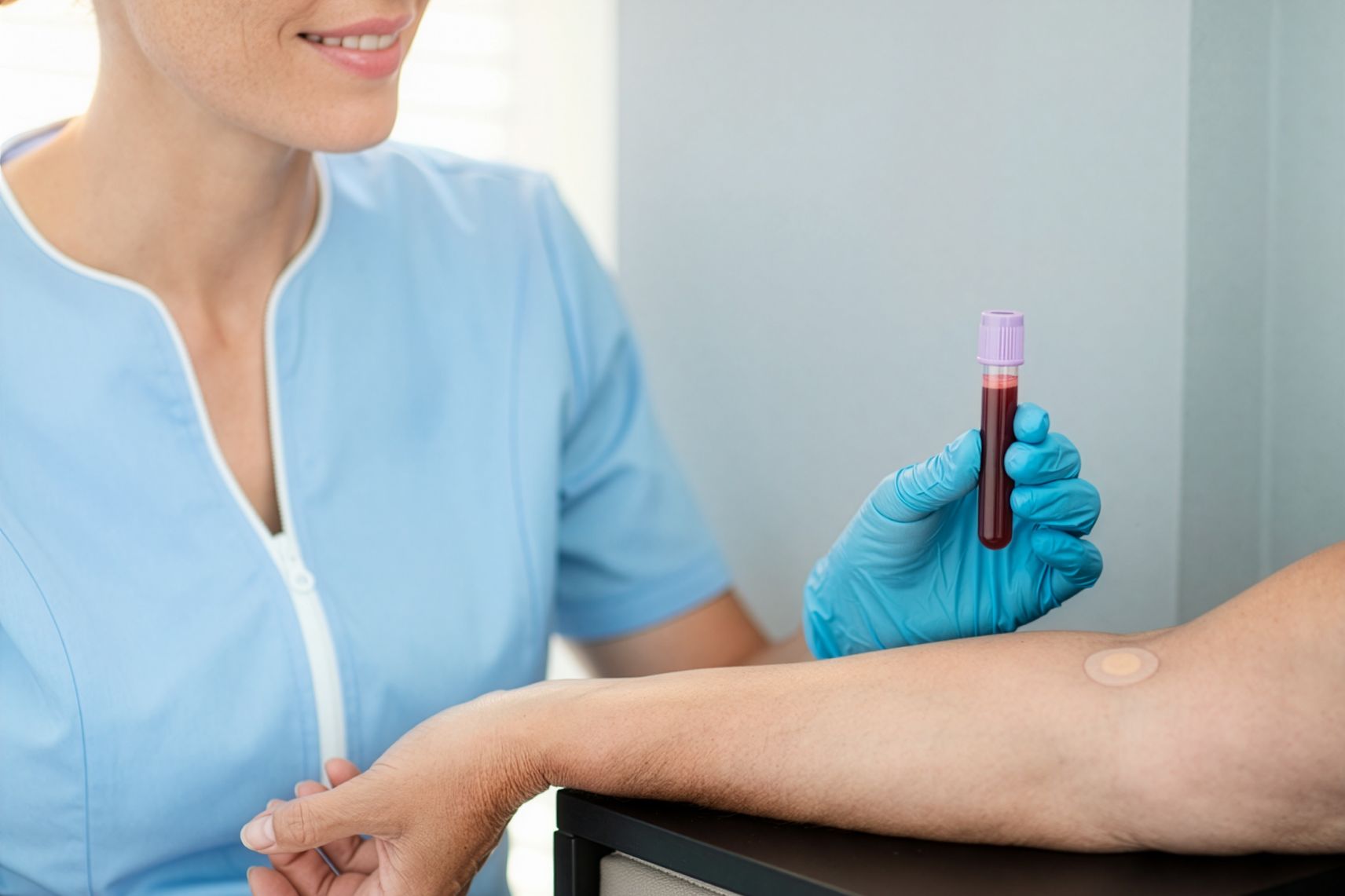 Provetta di sangue appena prelevata, tenuta dall’infermiera accanto al braccio del paziente